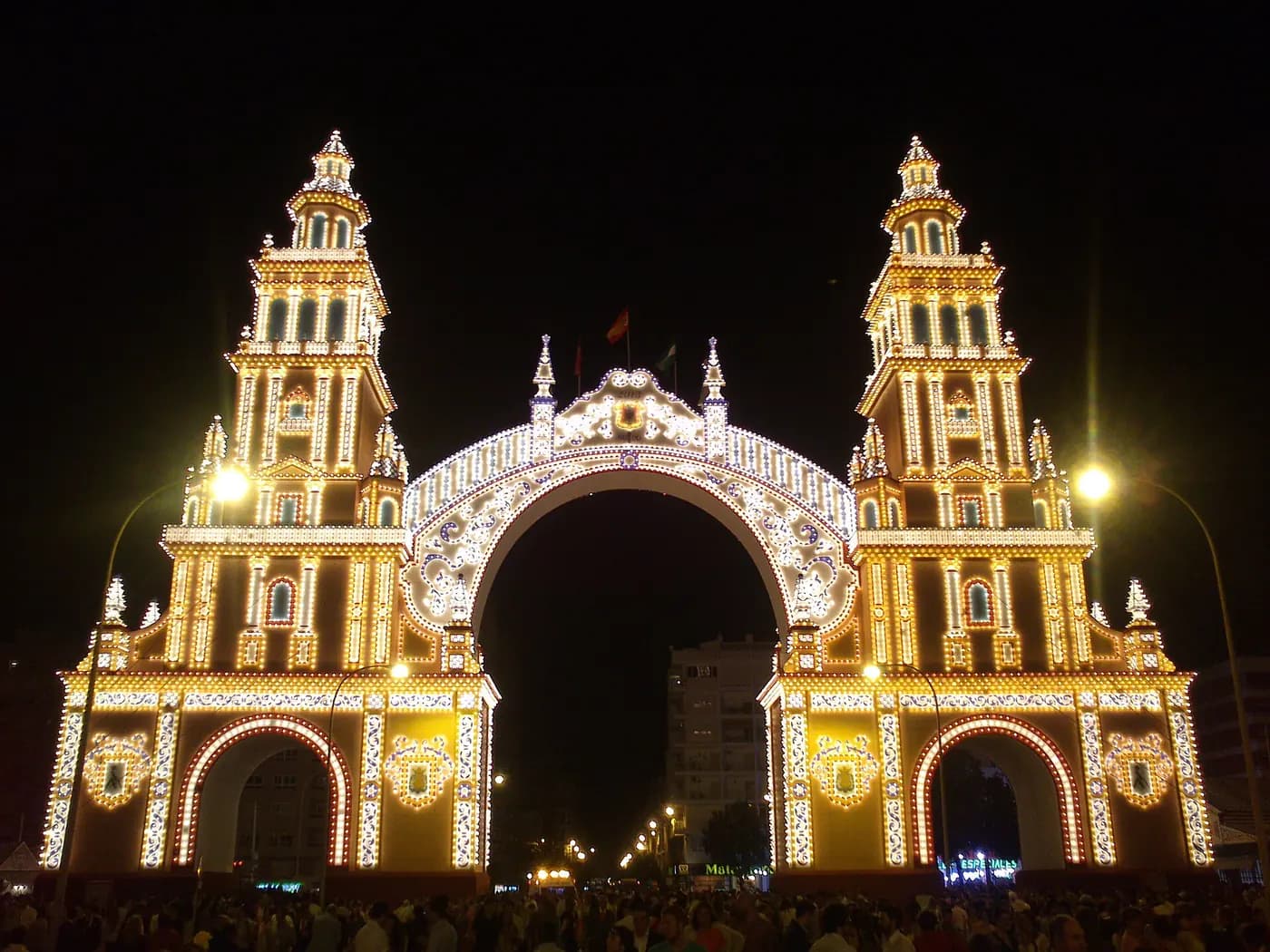 La portada iluminada de la Feria de Abril de Sevilla, con la multitud a sus pies
